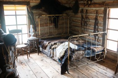 Cody, WY, USA - Jun 25, 2022: Old Trail Town is a tourist attraction with authentic frontier buildings from the late 1800's. Log cabin bedroom with bear furs as bedding. 