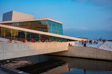 Oslo, Norveç, 20 Haziran 2023: Turistler, ziyaretçilere mermer kaplı çatısında yürüme olanağı sağlamak amacıyla 2008 yılında inşa edilen Oslo Opera Binası 'ndan gün batımını seyrediyorlar.. 