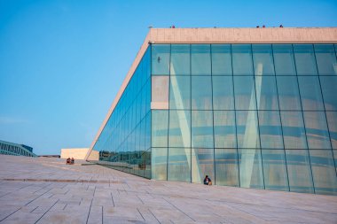 Oslo, Norveç, 20 Haziran 2023: Turistler, ziyaretçilere mermer kaplı çatısında yürüme olanağı sağlamak amacıyla 2008 yılında inşa edilen Oslo Opera Binası 'ndan gün batımını seyrediyorlar.. 