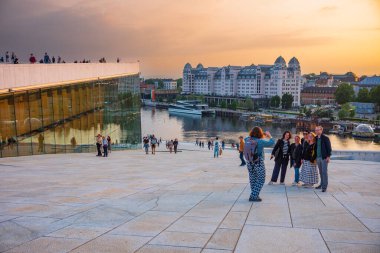 Oslo, Norveç, 20 Haziran 2023: Turistler, ziyaretçilere mermer kaplı çatısında yürüme olanağı sağlamak amacıyla 2008 yılında inşa edilen Oslo Opera Binası 'ndan gün batımını seyrediyorlar.. 