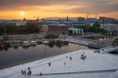 Oslo, Norveç, 20 Haziran 2023: Turistler, ziyaretçilere mermer kaplı çatısında yürüme olanağı sağlamak amacıyla 2008 yılında inşa edilen Oslo Opera Binası 'ndan gün batımını seyrediyorlar.. 