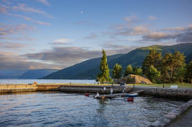 Balestrand, Norveç, 27 Haziran 2023: Sognefjord 'da yer alan hoş fiyort kasabası, günbatımında burada resmedilen küçük bir turistik kasabadır. Ay yükselirken bir aile rıhtımda oynar. 