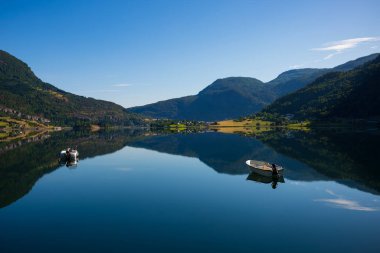 Norveç, Krossen yakınlarındaki Barsnesfjorden 'in durgun sularında, etrafındaki dağların fiyorda yansıtıldığı bulutsuz bir sabahta iki motorlu tekne yüzüyor.. 