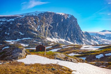 Kar, Norveç 'teki Jotunheimen Ulusal Parkı' ndaki Breiddalen Vadisi 'nde Geiranger yolu boyunca bir yaz günü boyunca zirve yaptı. Dağın eteğinde bir kulübe var.. 