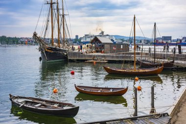 Oslo, Norveç - 21 Haziran 2023: Bygody Yarımadası kıyılarında dinlenen ve Oslo şehri bulutlu bir günde arka plan görevi gördüğü için iç Oslofjord 'da bulunan limandaki liman teknesi. 