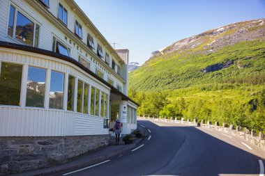 Geiranger, Norveç, 26 Haziran 2023: Bir turist, virajlı bir dağ yolunda bulunan Geiranger Fjord 'a tepeden bakan ünlü Utsikten Oteli' nin önünden geçiyor.. 