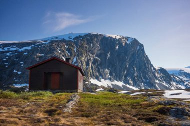 Kar, Norveç 'teki Jotunheimen Ulusal Parkı' ndaki Breiddalen Vadisi 'nde Geiranger yolu boyunca bir yaz günü boyunca zirve yaptı. Dağın eteğinde bir kulübe var.. 