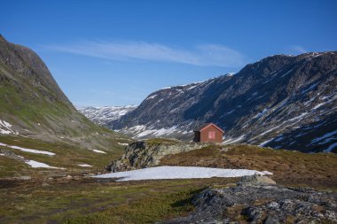 Kar, Norveç 'teki Jotunheimen Ulusal Parkı' ndaki Breiddalen Vadisi 'nde Geiranger yolu boyunca bir yaz günü boyunca zirve yaptı. Dağın eteğinde bir kulübe var.. 