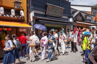 Kyoto, Japonya - 21 Haziran 2024: Kadınlar Kiyomizu Zaka 'yı ziyaret ederken kimono giyerler, dükkanlar, çay odaları ve yerel Kyoto tarzı mutfak ve hediyelik eşyalarla dolu bir alışveriş caddesi..