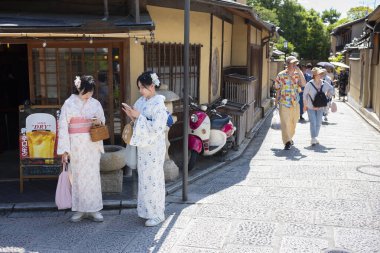 Kyoto, Japonya - 21 Haziran 2024: Kadınlar Kiyomizu Zaka 'yı ziyaret ederken kimono giyerler, dükkanlar, çay odaları ve yerel Kyoto tarzı mutfak ve hediyelik eşyalarla dolu bir alışveriş caddesi..