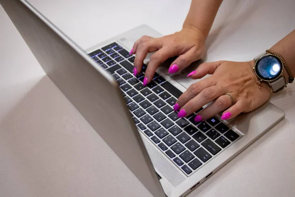 グレーの背景にラップトップのキーボードにタイピングピンクのネイルマニキュアで女性の手を閉じる ロイヤリティフリーのストック写真