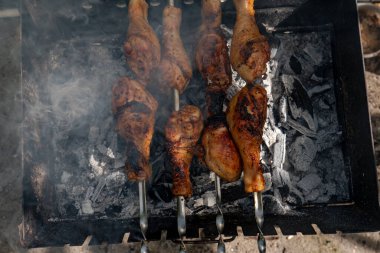 Chicken shanks on skewers on grill, grilling. clipart