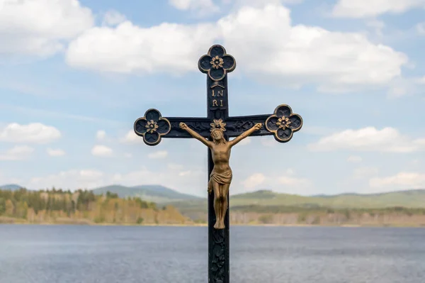 十字架 碑文Inriと十字架上のイエス キリストの像 水と背景の風景の中に 丘と白い雲と青い空 — ストック写真