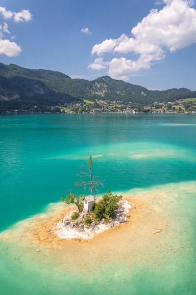 a small island with a chapel on the lake Wolfgangsee, the village of Sankt Gilgen and the mountains in the background, Alps, Austria