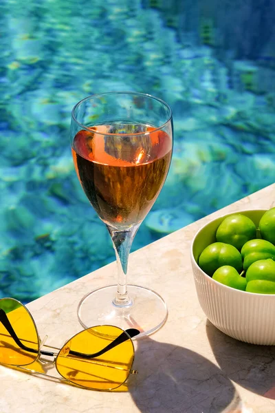 Glass of pink wine and yellow sunglasses at the pool. Summer holidays concept.