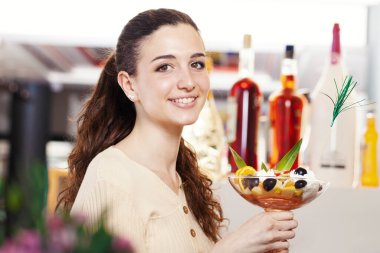 Kafe kafeteryasında, dondurmacıda ve pastanede üzerinde dondurma olan meyve salatasıyla gülümseyen güzel bir genç kadın. Esmer, ışıl ışıl bir kızın portresi gülüyor ve kameraya bakıyor..  