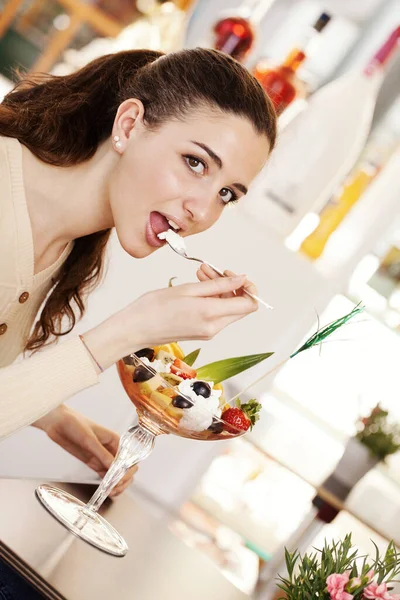 在咖啡店 冰激凌店和糕点店 年轻美丽的微笑的女人 一杯水果沙拉 上面有冰激凌 布鲁内特女孩吃奶油和看相机的肖像 — 图库照片