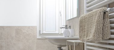 Modern banyo. Beyaz radyatörde sabun ve havluyla lavabo. Mermer ve bej seramik fayanslarla döşenmiş tuvalet. Işığın pencereden girmesiyle aydınlanan parlak oda, kopyalama alanı olan duvar
