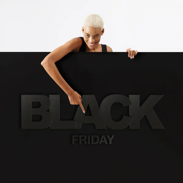 Black Friday shopping. Smiling black woman pointing at a Black Friday text on advertising banner commercial sign. Store and mall advertising Billboard guiding shoppers to deals