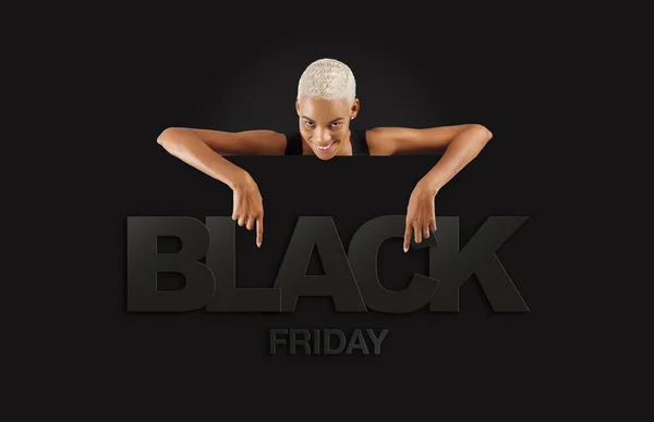 Black Friday shopping. Smiling black woman pointing at a Black Friday text on advertising banner commercial sign. Store and mall advertising Billboard guiding shoppers to deals