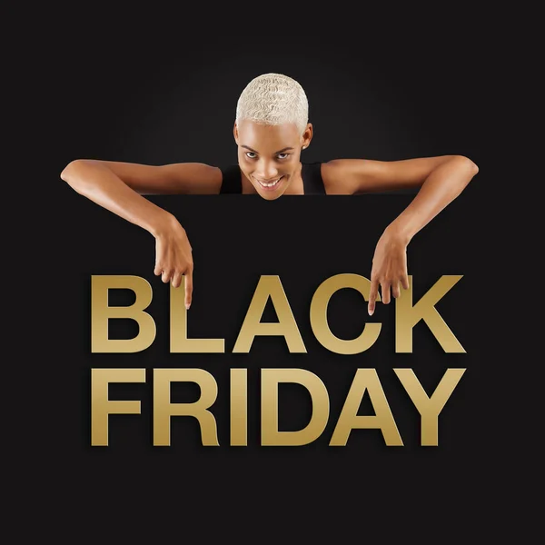 Black Friday shopping. Smiling black woman pointing at a Black Friday golden text on advertising banner commercial sign. Store and mall advertising Billboard guiding shoppers to deals