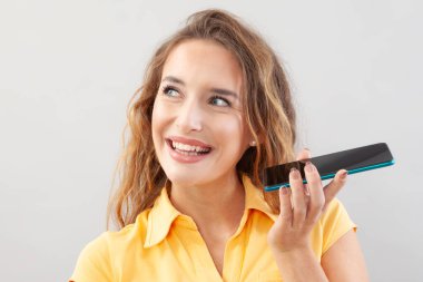 Neşeli ve güzel genç bir kadın cep telefonu kullanıyor, uzun saçlı, sarı bluz giyiyor. Beyaz arka planda, büyük mavi gözlü, gülen bir kızın portresi yan tarafa bakıyor..