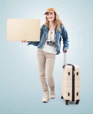 Gülümseyen ve boş bir karton tabela gösteren mutlu gezgin genç bayan turist otostop çekiyor. Mavi arka planda izole edilmiş. Yaz tatili ya da seyahat içeriği yaratıcısı kavramı