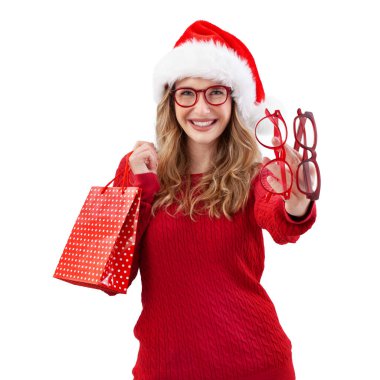 Gülümseyen Noel kadını kırmızı gözlük ve Noel Baba şapkası takıyor. Alışveriş torbası tutuyor ve beyaz arka planda izole edilmiş gözlük modelleri gösteriyor. Optisyen dükkanı veya internet mağazasından online alışveriş ve teklif