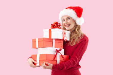 Neşeli bir kadın, elinde bir sürü kırmızı Noel hediyesi kutusu tutarken pembe arka planda izole edilmiş Noel Baba şapkası takıyor. Satılık tatil promosyonları, online alışveriş reklamları ya da hediye kartı için mükemmel.