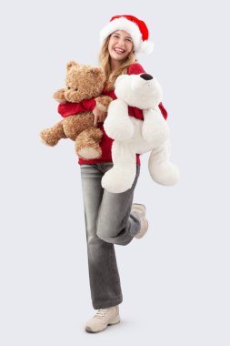 Mutlu Noeller, Noel Baba şapkası takan mutlu ve neşeli genç kadın gülümserken oyuncak ayıları şefkatle kucaklıyor ve onları sıkıca kollarına alıyor. Beyaz arka planda izole edilmiş.