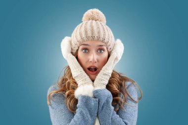 Kış Noel 'inde kendini kucaklayan harika bir kadın. Samimi mavi bir kazak, ponpon şapkası, kulak ısıtıcı, eşarp ve eldiven giyiyor. Kameraya gülümsüyor, mavi bir arka planda izole edilmiş.