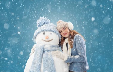 Kışın kar yağarken sıcak kış kıyafetleri içinde kardan adam yapmaktan zevk alan mutlu genç bir kadın. Kış mevsiminde Noel tatili boyunca kayak gezisi. Soğutma ve ısıtma sıcaklığı kavramı