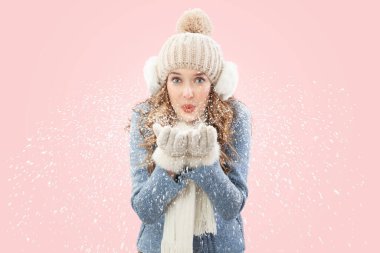 Mutlu genç bir kadın pembe arka planda izole edilmiş kameraya bakarak ellerinden kar üflüyor. Kış mevsiminde Noel tatili. Soğutma ve ısıtma sıcaklığı kavramı