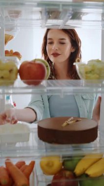 Mutlu, gülümseyen kadın buzdolabını açıyor ve parmağını kullanarak çikolatalı pasta ve krema tadıyor. Tattan zevk alıyor, görünüşe göre zevkten zevk alıyor. Mutfak dolabının içinden pov çekimi.