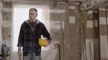 İnşaat işçisi güvenlik kaskı takıyor, sert şapkayı yumruk ve çekiçle vuruyor, güven ve koruma gösteriyor, işyeri güvenliği ve kişisel koruma ekipmanlarını vurguluyor, PPE