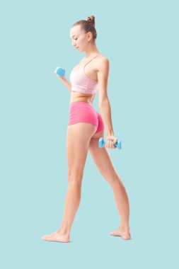 Fitness egzersizi için küçük dambıllarla duran genç bir kadın. Sağlıklı yaşam tarzı, dayanıklılık eğitimi, sağlık ve aktif yaşam konsepti. Arka plan görünümü mavi arkaplanda izole edildi
