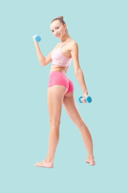 Spor yapmak için küçük dambılları olan gülümseyen genç bir kadın. Sağlıklı yaşam tarzı, dayanıklılık eğitimi, sağlık ve aktif yaşam konsepti. Arka plan görünümü mavi arkaplanda izole edildi