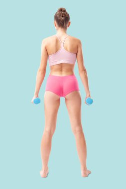 Fitness egzersizi için küçük dambıllarla duran genç bir kadın. Sağlıklı yaşam tarzı, dayanıklılık eğitimi, sağlık ve aktif yaşam konsepti. Arka plan görünümü mavi arkaplanda izole edildi