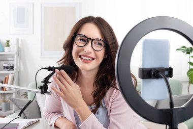 Gülümseyen genç bayan içerik yaratıcısı ve sözü geçen kişi akıllı telefon ve halka ışığıyla mikrofona konuşuyor. Sosyal medya için canlı yayın, podcast veya kayıt videoları ve içeriği