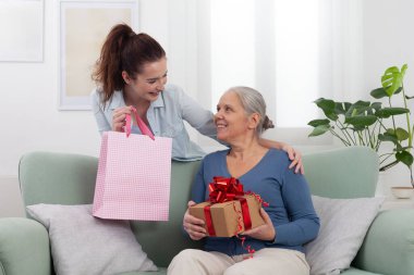 Memlekette mutlu çok nesilli aile anları. Gülümseyen genç bir kadın ya da torun neşeli yaşlı anne ya da büyükannesine hediye veriyor. Anneler Günü 'nü ya da özel bir günü kutluyor.