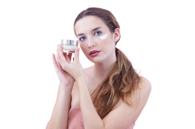 Cilt nemlendirici süren ve kameraya bakarken bir kavanoz krem tutan genç bir kadın. Cilt bakımı ve güzellik anlayışı. Arka planda izole edilmiş. Yüz bakımı, makyaj ve sağlıklı cilt