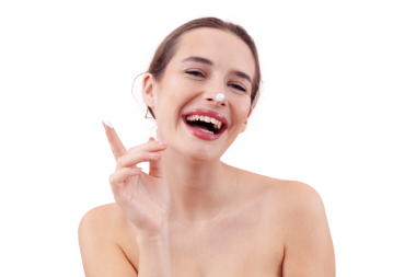 Cilt nemlendirici kremi sürerken gülümseyen genç bir kadın. Parmağında ve burnunun ucunda güzellik kremi var. Arka planda izole edilmiş. Yüz bakımı, makyaj ve sağlıklı cilt