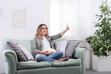 Akıllı gözlük takan, elinde patlamış mısır tutan bir kadın sanki sanal bir ekranla etkileşiyormuş gibi parmağıyla işaret ediyor. Evdeki dijital eğlencenin tadını çıkarıyorum. Gelecekçi teknoloji