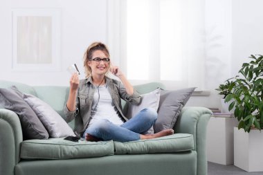 Akıllı gözlük takan gülümseyen genç bir kadın. Sanal ekrana bakarken gözlük kontrolüne dokunuyor ve elinde kredi kartları tutuyor. Dijital ödeme ve online alışveriş, teknoloji yaşam tarzı