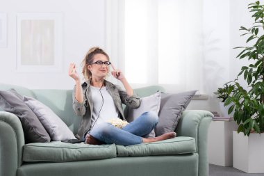 Akıllı gözlük takan, elinde patlamış mısır tutan bir kadın sanki sanal bir ekranla etkileşiyormuş gibi gözlüklerine dokunuyor. Evdeki dijital eğlencenin tadını çıkarıyorum. Gelecekçi teknoloji konsepti