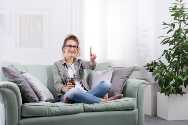 Genç bir kadın evde akıllı gözlükler takıp kanepede otururken ve elinde bir şişe şurup tutarken ekrana dokunuyor. Teletıp, e-sağlık ve dijital reçete kavramı