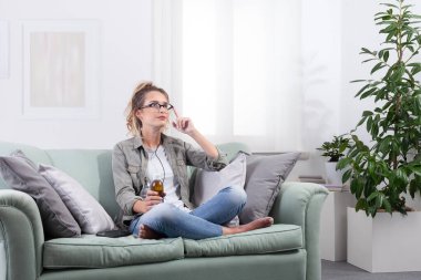 Evde akıllı gözlükler takan bir kadın arayüz kontrolüne dokunuyor ve sanal ekrana bakarken elinde bir ilaç şişesi tutuyor. Teletıp, e-sağlık ve dijital reçete kavramı