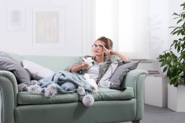 Kanepede uzanmış, akıllı gözlük takan ve tıbbi yardım almak için sanal ekranla etkileşime geçen hasta bir kadın. Teletıp, soğuk algınlığı, grip ve dijital sağlık çözümleri kavramı