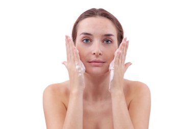 Yüzünü köpük temizleyiciyle temizleyen, ellerini köpükle kaplayan ve cildine süren genç bir kadın. Temiz ve sağlıklı yüz için cilt rutini. Beyaz arka planda izole edilmiş, akne bakımı