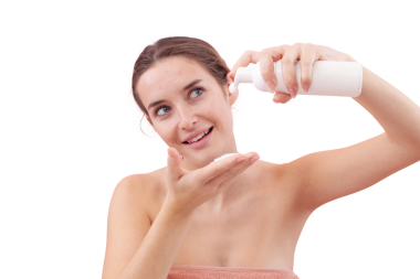 Gülümseyen genç bir kadın yüzünü yıkamadan önce eline köpüklü yüz temizleyici sürüyor. Temiz ve sağlıklı cilt için cilt rutini. Beyaz arka planda izole edilmiş. Sivilce, güzellik konsepti.